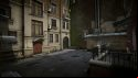 Escape from Tarkov screenshots: The back side of a residential building downtown, with a hopscotch pattern chalked in pink around a manhole cover and graffiti covering a low shed by a high brick wall