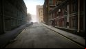 Escape from Tarkov screenshots: An empty city street, with a red building with white trim on the right and a blue building on the left. The street disappears in the mist in the distance, and two crashed cars can be seen near the intersection ahead