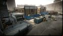 Escape from Tarkov screenshots: A parking area and loading dock, with a dumpster filled with construction debris in the centre. Crashed and burned vehicles can be seen on the far side, and a heap of trash bags is piled up near the entrance to a garage on the near side
