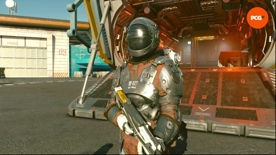 A person covered head to toe in a space suit made from the toughest materials, making it great for the best Starfield tank build. They're beside their spaceship hangar.