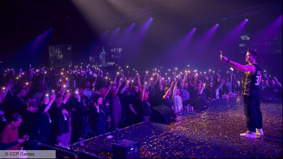 A man stands on stage encouraging the Eve Online community to light their phones up