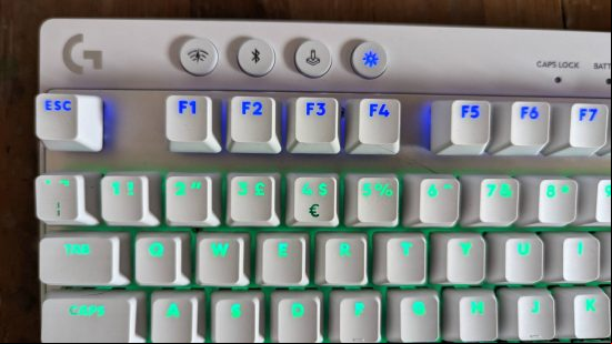 Logitech G Pro X TKL Lightspeed review: the top left of a white keyboard with blue and turquoise RGB lighting is shown above a wooden worktop.