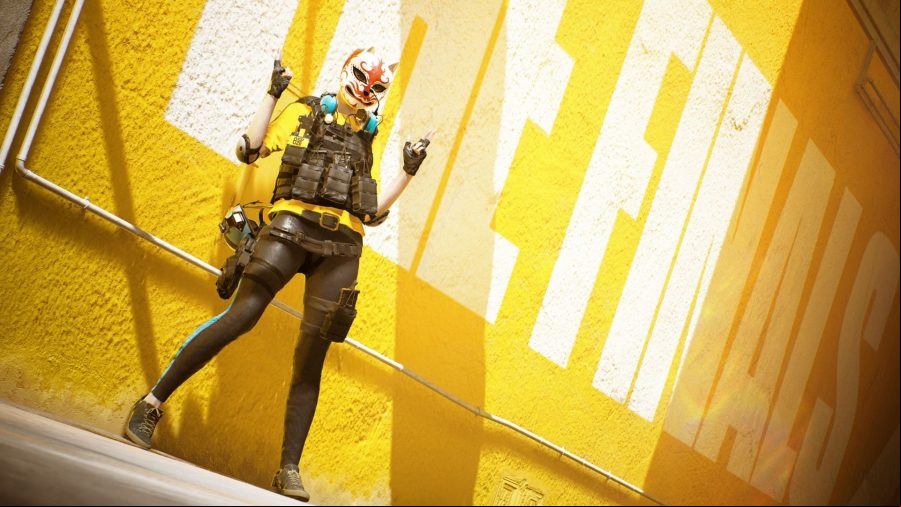 A character in yellow and black outfit with a cat mask on stands in front of a yellow wall reading the finals