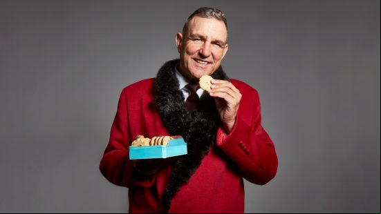 World of Tanks Vinnie Jones: Vinnie Jones eats a biscuit while wearing a red coat.