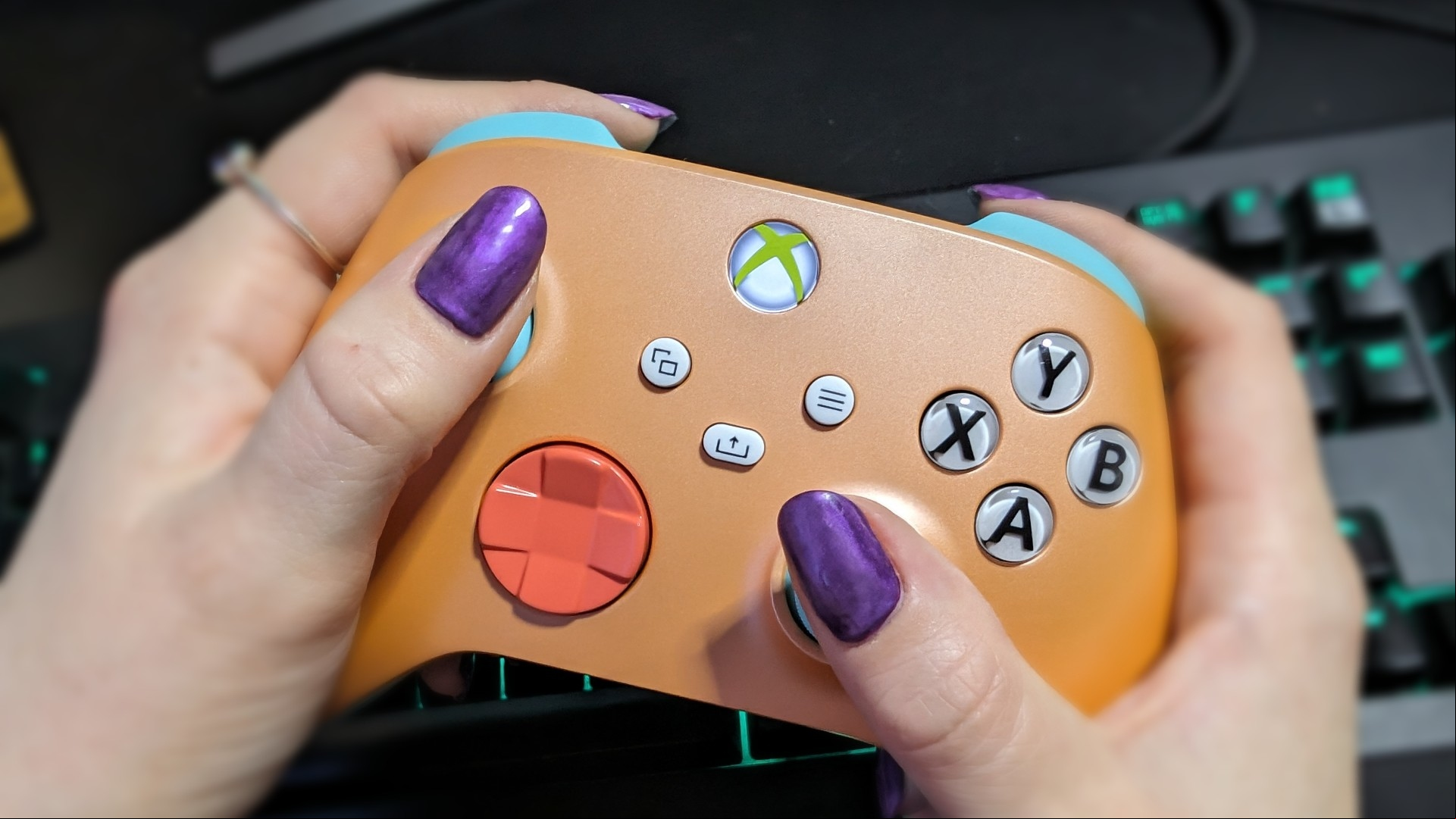 Xbox Wireless Controller review image showing two human hands holding the controller above a keyboard.